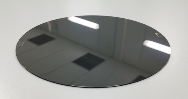 Polished germanium semiconductor wafer with mirror-like dark metallic finish on white surface