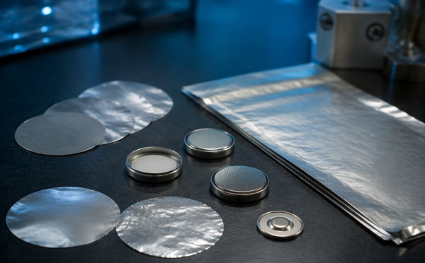 Stainless foil discs beside coin cell components on a laboratory bench