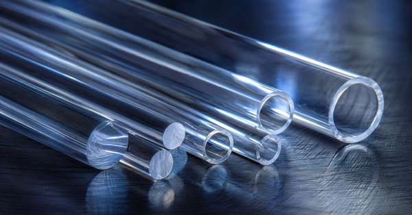 Assorted clear fused quartz tubes and solid rods catching cool blue light on a dark metal surface.