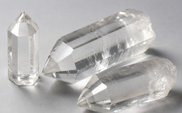 Clear synthetic quartz single crystals with pointed hexagonal terminations on a grey surface.