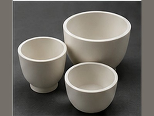 Three white ceramic crucibles of different capacities grouped on a dark background.