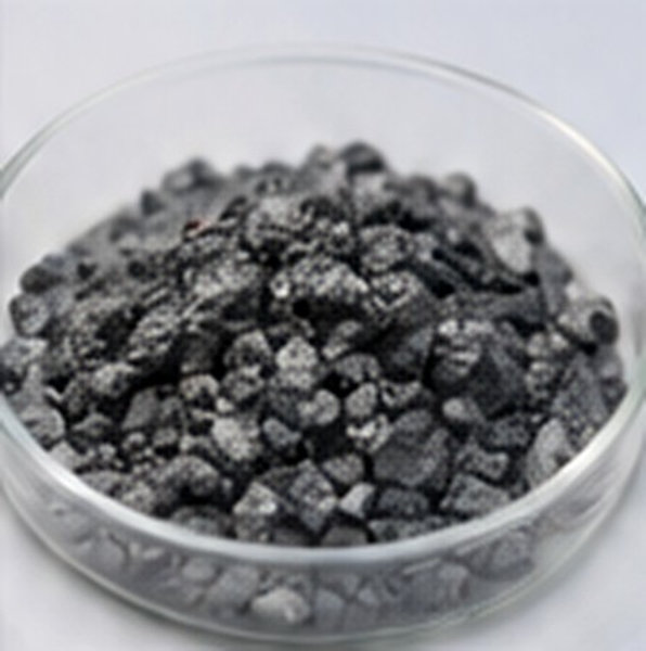 Dark metallic granules are grouped in a clear dish for thin-film vacuum deposition.